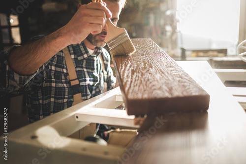 Craftsman painting a wooden board by paintbrush in his carpentry workshop