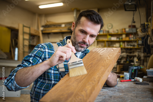 Craftsman applies varnish on wooden board by paintbrush in his carpentry work...
