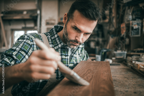 Craftsman applies varnish on wooden board by paintbrush in his carpentry work...