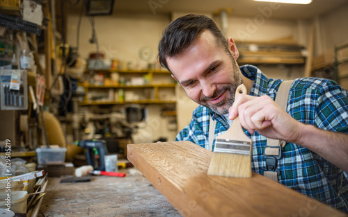 Craftsman applies varnish on wooden board by paintbrush in his carpentry work...