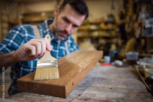 Craftsman applies varnish on wooden board by paintbrush in his carpentry work...