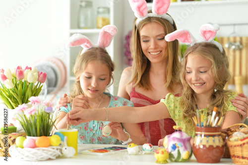 Mother with daughters wearing rabbit ears decorating Easter eggs