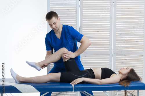 The orthopedic doctor makes a diagnosis of the muscle tone on the girl's legs. Manual therapy
