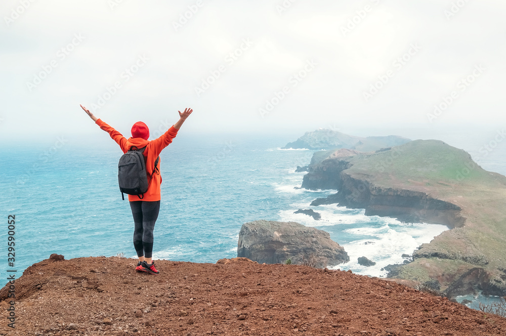 Trail backpacker woman dressed orange sporty hoodie enjoying Atlantic ocean bay view on Ponta de Sao Lourenço peninsula -the easternmost point of Madeira island, Portugal