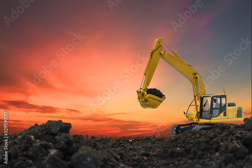 Excavators are digging the soil in the construction site on the orange sky background