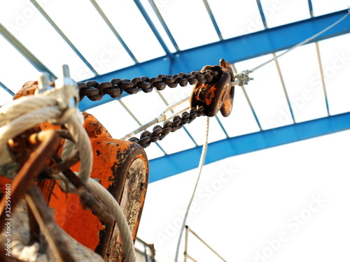 Chain hoist or lifting hook equipment. Bracing the sling to fasten the blue steel frame in the blurred construction site. On the background of a white sky. Selective focus
