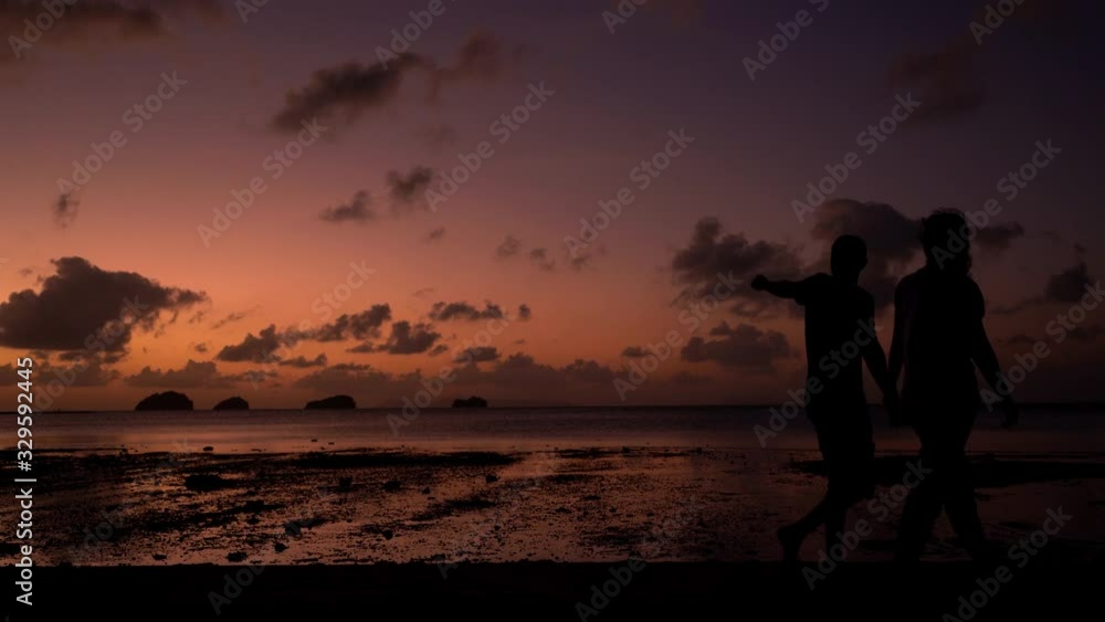 A couple walks along a tropical beach at sunset. Bright colors of the sunset. Romantic atmosphere A couple walks along a tropical beach at sunset. Bright colors of the sunset. Romantic atmosphere