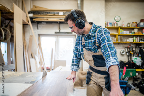 Carpenter using circular saw to cut a large wooden board at carpentry workshop