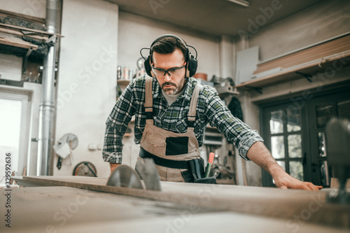 Carpenter using circular saw to cut a large wooden board at carpentry workshop