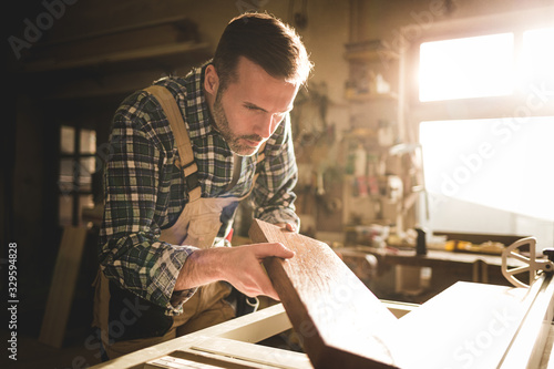 Carpenter in carpentry workshop looking at wooden board and checking his work