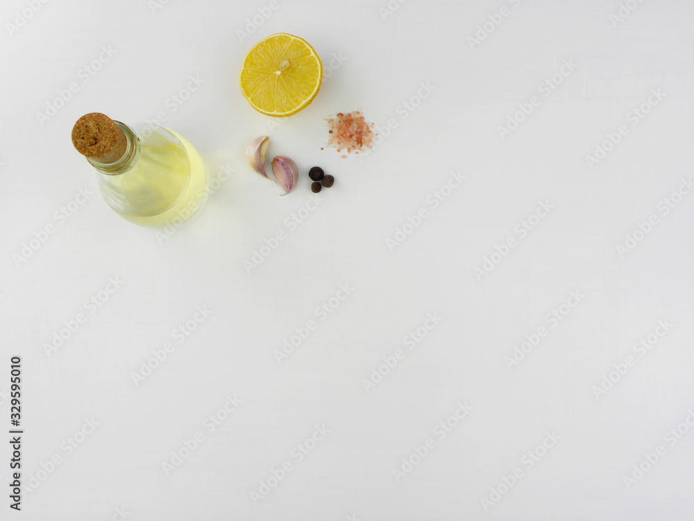 half ripe lemon, oil in a glass bottle, two cloves of garlic, grains of pepper and pink salt on a white background half ripe lemon, oil in a glass bottle, two cloves of garlic, grains of pepper and pink salt on a white background