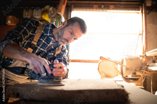 Carpenter at workshop polishes wooden board with a electric orbital sander photo