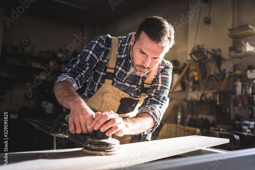 Carpenter at workshop polishes wooden board with a electric orbital sander
