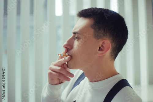 Portrait of a man smoking in a smoking cubicle. Cigarette smoking area. A man smokes in a glazed room.
