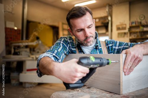 Carpenter at workshop drilling a hole by drill in a wooden board