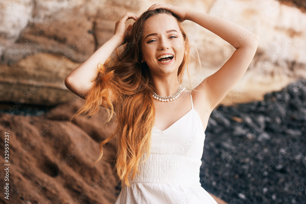 Gorgeous girl in a long white dress on the ocean at the beach. The model is inherited by nature laughing, having fun, going crazy. Happy girl on vacation, summer, emotions. The bride on vacation.