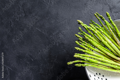 Fresh baby green asparagus in a colander. Black background. Top view. Copy space
