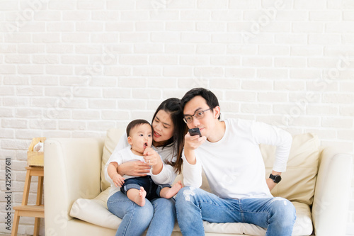 The concept of a happy family. Asian families consist of parents and baby sitting on the sofa watching TV happily. Family holiday