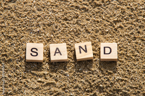 SAND word created with hipster style vintage board game wooden letters on sand beach background. Oblique sun rays shining on the letters creating shadows.