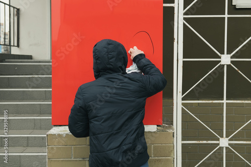 Photos Unknown man in blue jacket with a hood removes stains left by vandals from his store