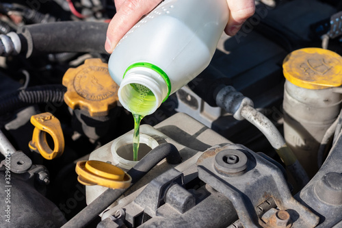 Fotografija Hand with bottle pouring antifreeze coolant into the expansion tank