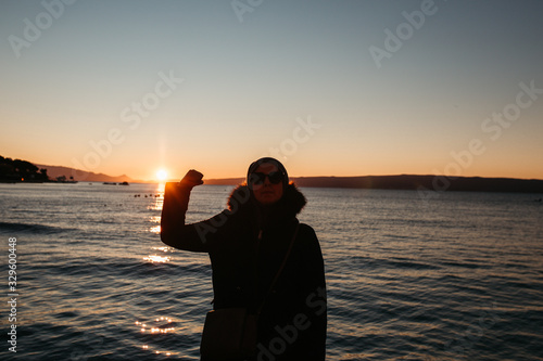 photo of young European Muslim women with hijab standing and looking into sea. She is standing turned back with her hands in the air. She is happy and relaxed. Photos taken during sunrise.  