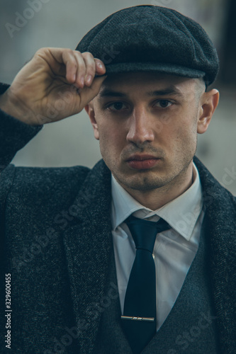 Portrait of a man in the image of an English retro gangster dressed in a coat, suit and flat cap.