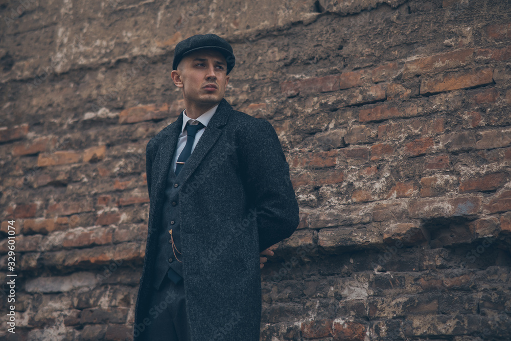 A man posing in the image of an English retro gangster near brick wall. A man posing in the image of an English retro gangster near brick wall.