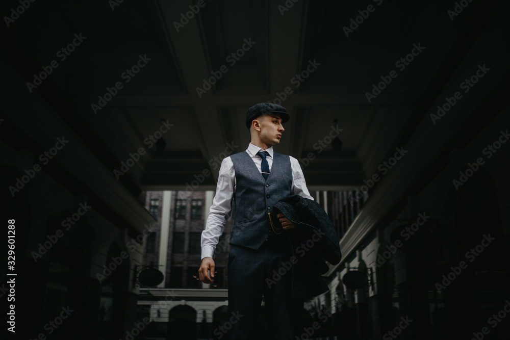 A man posing in the image of an English retro gangster in Peaky blinders style at city street.