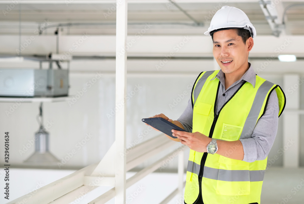 Engineers man standing in the site and holding tablet with copy space. Feeling happy on finish work. Wearing safety helmet. Engineering and construction concept. Engineers man standing in the site and holding tablet with copy space. Feeling happy on finish work. Wearing safety helmet. Engineering and construction concept.