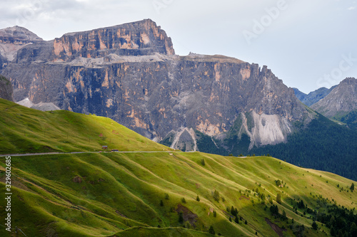 Sella mountain group in Dolomites, Italy, at sunset, with rays of light across green layers of grass.