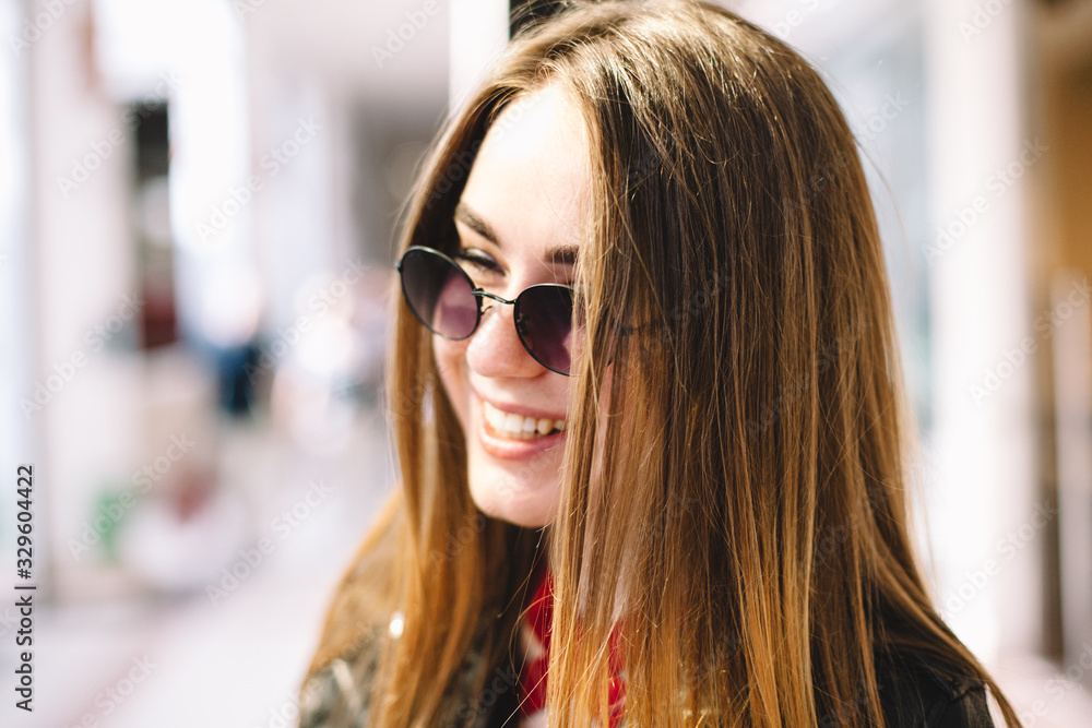 Portrait of happy smiling young woman wearing sunglasses standing in shopping mall Portrait of happy smiling young woman wearing sunglasses standing in shopping mall