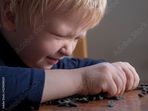 small blond child sits at table sorting out sunflower seeds. kid comes up with entertainment and actively learns necessary skills