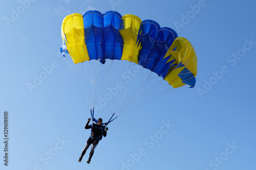 Skydiver is piloting a blue-yellow parachute.