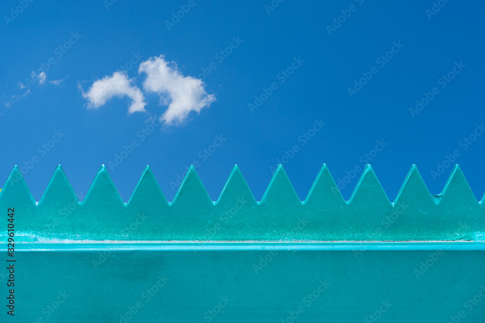 Zaun mit scharfen Zacken und im Hintergrund blauer Himmel mit Wolke