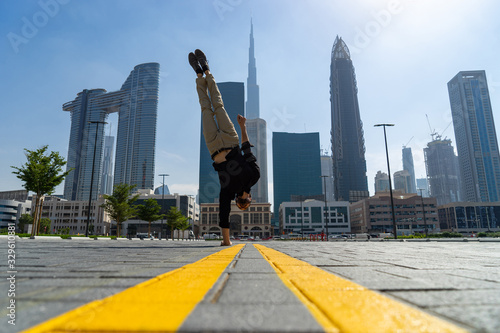 Flexible Acrobat keep balance on one hand with blurred Dubai cityscape. Concept of modern and healthy lifestyle photo