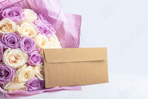 Bouquet of fresh amazing white and purple roses and craft envelope. Gift for holiday Mother's, Valentine's day, birthday, anniversary and Wedding. Gift Wrapping Concept. Copy space for text.