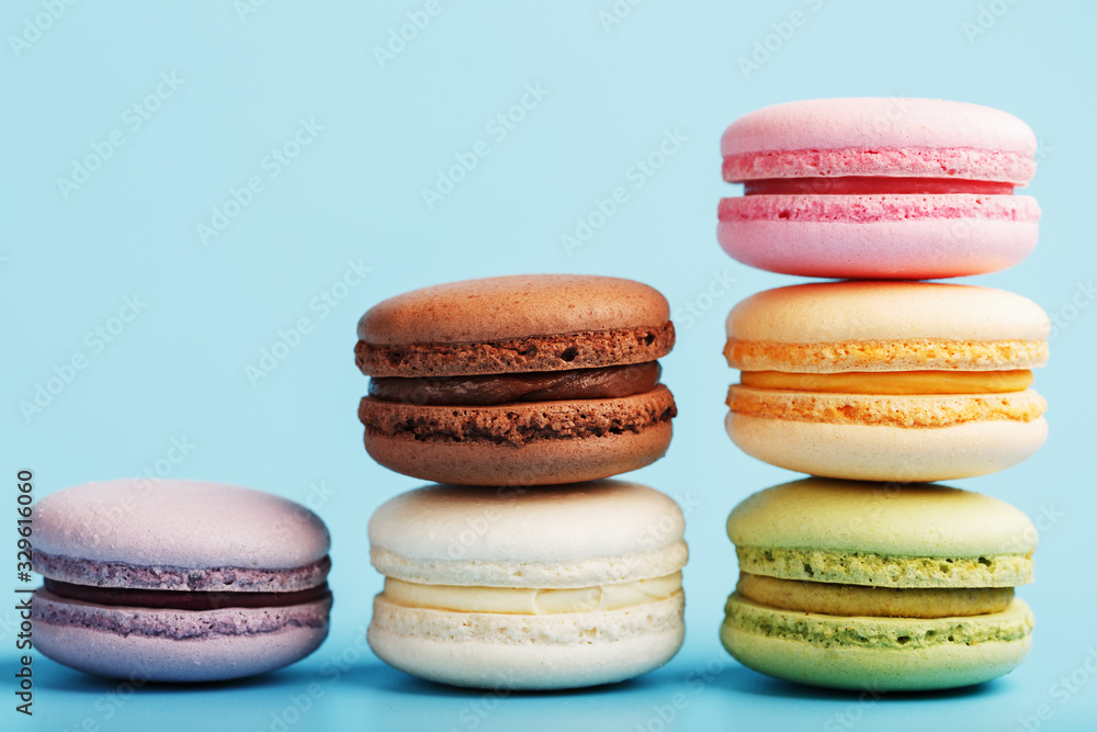 Multicolored French macaroni macaroni cookies are arranged in a pyramid on a blue background. Multicolored French macaroni macaroni cookies are arranged in a pyramid on a blue background.