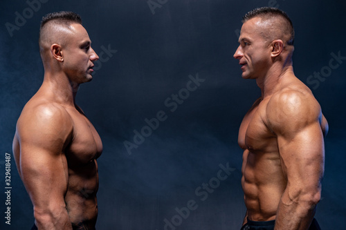 Two Muscular man standing against each other isolated on the black background. Concept of confrontation and fight