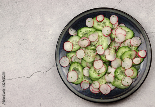 Cucumber and radish salad in a plate on a light background. Top view, flat lay