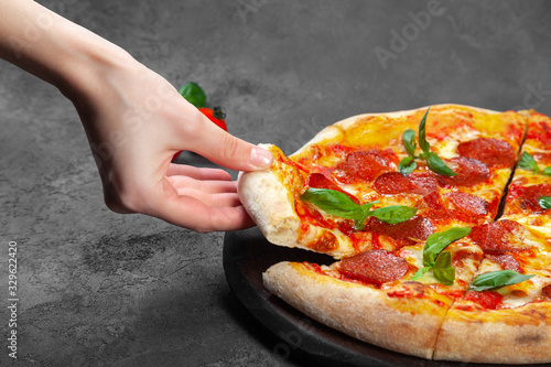 Female hand take slice of pepperoni pizza with basil