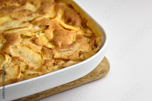 Apple pie, dessert from stewed fruits in ceramic dish for baking in the oven, closeup. Charlotte on wooden cutting board on white background