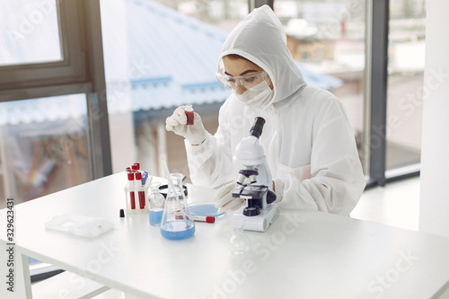Laboratory worker in coverall suit is adjusting microscope. The researcher is doing coronavirus testing in a modern laboratory with solutions on the table. photo