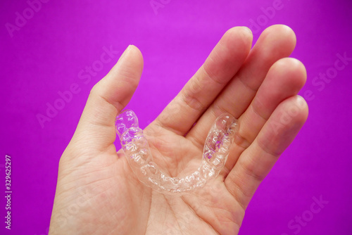 hand holding clear plastic retainer teeth that isolated on purple background. it's an equipment for orthodontist give the patient to orthodontic surgery in dental clinic or hospital