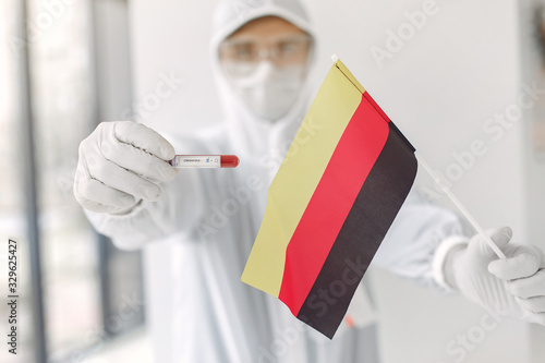 The scientist in coverall suit with a coronavirus sample and German flag.