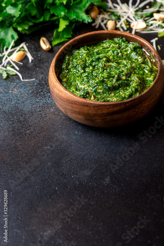 Homemade pesto sauce in a wooden bowl and ingredients for cooking on a black background close-up, free space for text. Italian food, copy space.