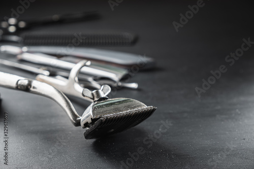 On a black dusty surface are old barber tools. Vintage manual hair clipper comb razor shaving brush shaving brush hairdressing scissors. black monochrome