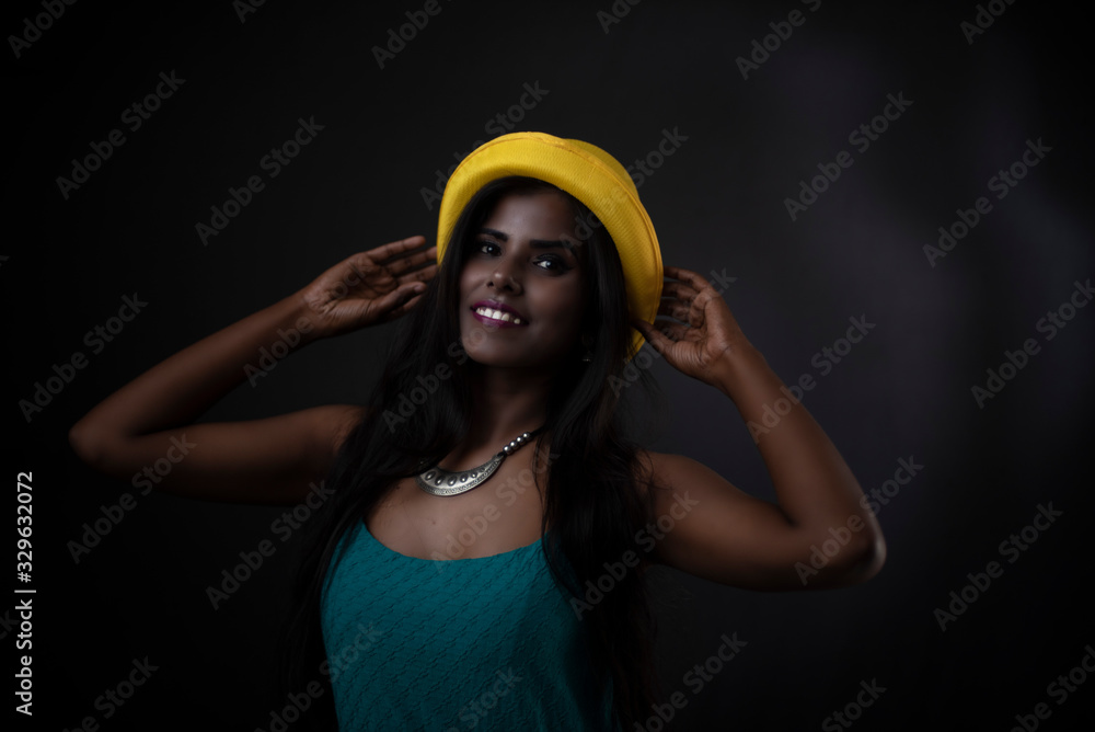 Fashion portrait of young dark skinned Indian/African brunette girl in green western dress, jewelry and yellow hat in front of black copy space studio background. Indian fashion photography. Fashion portrait of young dark skinned Indian/African brunette girl in green western dress, jewelry and yellow hat in front of black copy space studio background. Indian fashion photography.