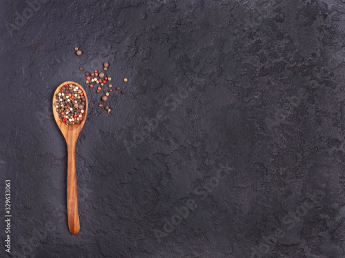 Colored pepper on a wooden spoon on a black concrete background