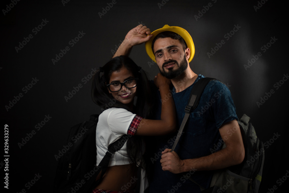 A dark skinned Indian/African girl in school uniform and a Kashmiri/European/Arabian man in casual wear and hat with bag pack in front of black copy space studio background. Indian lifestyle. A dark skinned Indian/African girl in school uniform and a Kashmiri/European/Arabian man in casual wear and hat with bag pack in front of black copy space studio background. Indian lifestyle.